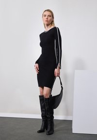 Abito nero aderente con strisce bianche ai lati, maniche lunghe e texture a coste. Abbinato a stivali di pelle nera al ginocchio e una borsa nera.