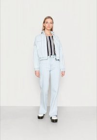 Jaqueta de denim azul claro cropped e jeans flare combinando com riscas verticais, acompanhados de uma blusa com riscas em preto e branco. Sapatos pretos chunky.