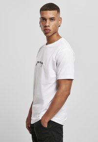 Balta medvilninė marškinė su apvaliu iškirpimu ir trumpomis rankovėmis, su juodais kursyviais rašmenimis priekyje, pasižyminti laisvu kirpimu.