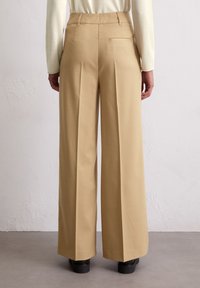 Beige pantalon met wijde pijpen, gemaakt van een gladde stof, met voorplooien en een achterzak, afgewerkt met een nette zoom en een subtiele glans.