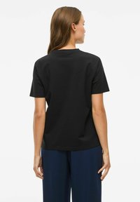 Zwarte katoenen T-shirt met korte mouwen, ronde hals en een losse pasvorm, van de achterkant weergegeven, met een gladde textuur en eenvoudig ontwerp.