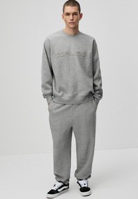 Szary sweatshirt i pasujące dresy, wykonane z miękkiego materiału, zdobione teksturowanym logo 'COALITION', z luźnym krojem i elastycznymi mankietami.