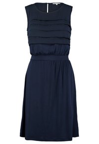 Robe bleu marine sans manches, longueur au genou, avec un corsage à volants, une taille cintrée et une fente latérale sur fond blanc.