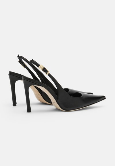 Sorte slingback-højhælede sko i læder med spidse tæer og remme med guldlås, vist fra siden på hvid baggrund.