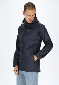 Marineblauwe waterdichte jas met een ritssluiting aan de voorkant, verstelbare capuchon en zijzakken. Gladde textuur met minimale branding op de borst.