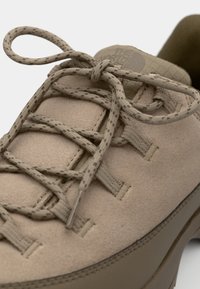 Beige ruskind sneakers med strukturerede snørebånd med prikkede detaljer, en polstret krave og en gummisål med afrundede kanter.