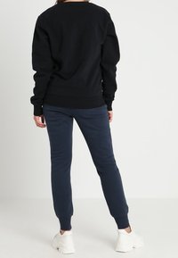 Sudadera negra con escote redondo, puños acanalados y un corte holgado, combinada con pantalones de chándal azul marino. Zapatillas gruesas blancas completan el look.