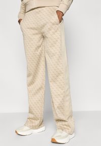 Παντελόνια φόρμας μπεζ με γεωμετρικό σχέδιο, πλαϊνές ρίγες και τσέπες. Κατασκευασμένα από μαλακό ύφασμα, διαθέτουν άνετη εφαρμογή.