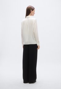 Cream-colored satin shirt with long sleeves and a collar, paired with high-waisted black wide-leg pants, showcasing a smooth texture and elegant design.