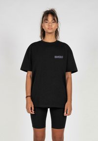 Sort bomulds t-shirt med korte ærmer, der har et lille grafisk motiv på brystet. Kombineret med sorte knælange cykelshorts.