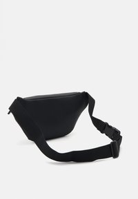 Sac en néoprène noir en bandoulière avec une forme courbée, une sangle réglable et un système de fermeture à clip durable. Texture lisse, design minimaliste.