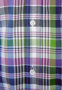 Geruit overhemd met paars, groen en blauw ruitpatroon. Gemaakt van lichtgewicht stof, het heeft een knoopsluiting en witte knopen.