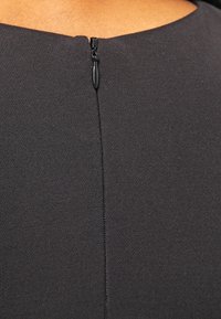 Robe en tissu noir avec un décolleté en forme de scoop subtile et un discret détail de fermeture éclair au dos, possédant une surface lisse et texturée.