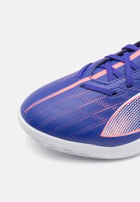 Buty sportowe z niebieską teksturowaną cholewką z różowymi akcentami i paskami, białą gumową podeszwą oraz siateczkowym panelem bocznym zapewniającym wentylację.