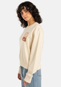 Beige sweatshirt met een ronde halslijn, ribgebreide mouwen en onderkant. Heeft een grafische print van een strandscène in vervaagde oranje tinten.