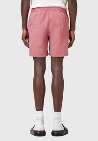 Lyserøde shorts lavet af letvægtsstof, elastisk talje, sidelommer og baglommer, samt et afslappet design, vist fra ryggen.