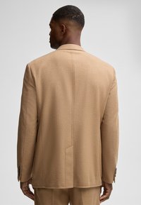 Beige Wolle Blazer mit strukturiertem Design, mittigen Schlitz und Knopfmanschetten, das eine glatte Textur und eine taillierte Passform zeigt.