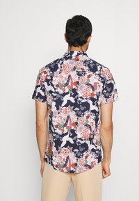 Korte mouwen, marineblauw shirt met een bloemen- en kraanvogelpatroon in tinten roze en rood, gemaakt van lichtgewicht stof met een ontspannen pasvorm.