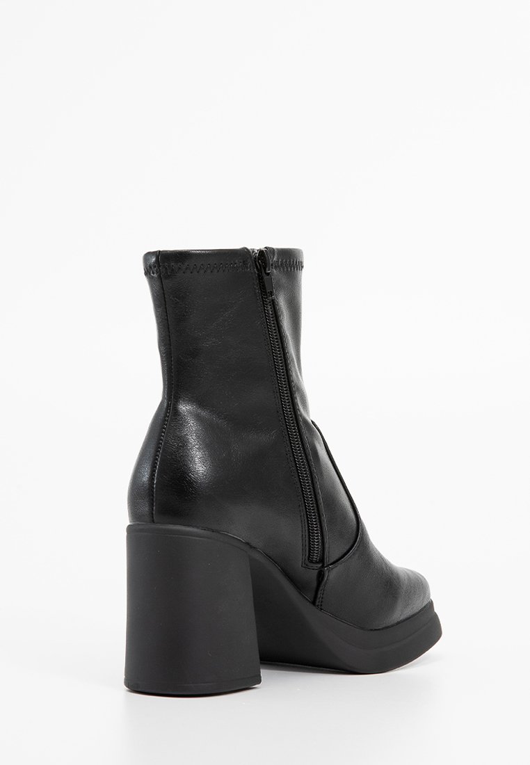 Bottine en cuir noir avec un haut talon carré, fermeture éclair sur le côté, texture lisse et détails de coutures.