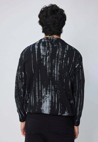 Pull noir en tricot avec un motif de coups de pinceau en gris. Le design comprend une coupe décontractée et des poignets côtelés.