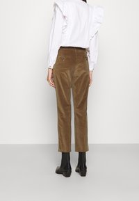 Bruine corduroy broek met een getailleerde pasvorm, zijzakken en een subtiele glans, gecombineerd met een witte blouse met ruches.