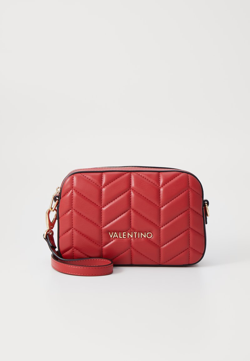 Red quilted leather bag with a chevron pattern, gold logo, zip closure, and a detachable strap. Smooth texture and rectangular shape.