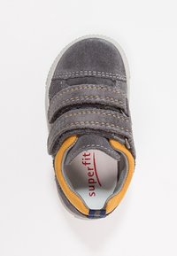 Scarpa in suede grigia per bambini con rifiniture gialle e due cinturini in velcro, suola bianca e branding "superfit" rosso all'interno.