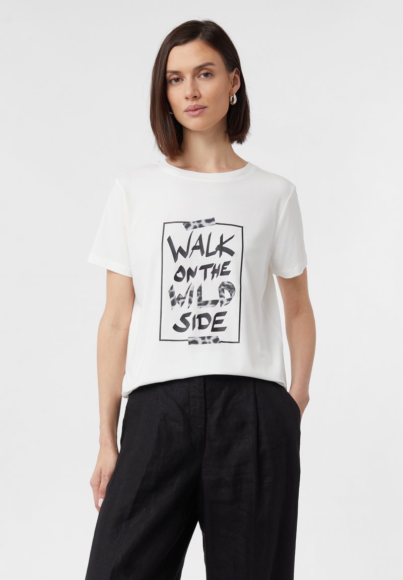 T-shirt en coton blanc à manches courtes avec un design graphique en texte noir "WALK ON THE WILD SIDE" à l'intérieur d'un cadre rectangulaire.