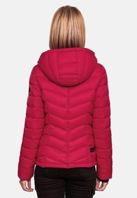 Red insulated puffer jacket with a hood, featuring chevron stitching and a black logo tag on the left side, worn over dark pants.