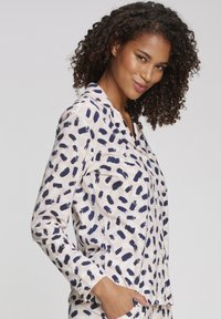 Lichte, lange mouwen pyjamablouse met een marineblauw penseelstrekenpatroon op een lichte achtergrond, voorzien van een kraag en een knoopsluiting aan de voorkant.