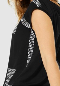 Chemise noire à manches courtes avec un motif de flèches blanches sur les côtés. Fabriquée en tissu doux avec une coupe décontractée.