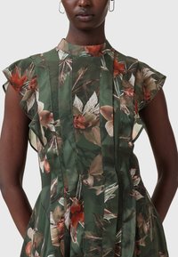Green floral dress with cap sleeves, featuring textured fabric, vertical pleats, and a high neckline. Floral pattern in shades of red and cream.