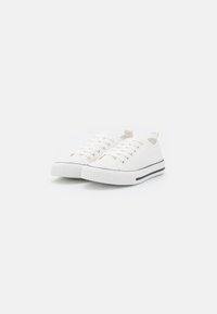 White canvas sneakers with round toe, lace-up design, rubber sole, and black horizontal stripe along the base. Smooth texture throughout.