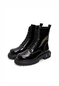 Musta lakattu nahkasaapas, jossa on nauhoitus ja paksu kumipohja, sisältää koristeellisia kultasävyisiä metalliosia ja korkean nilkkasuunnittelun.