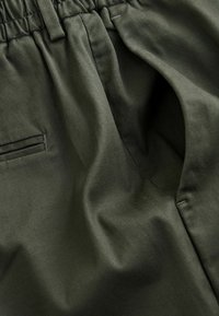 Gros plan sur un tissu vert foncé avec une taille élastique et une poche latérale sur un pantalon.