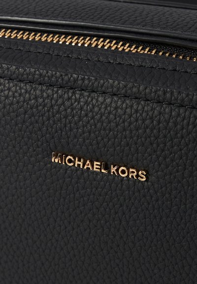 Sac à main en cuir texturé noir avec des accessoires en métal doré. Il dispose d'une fermeture éclair et d'un logo de marque embossé, mettant en avant un design épuré et minimaliste.