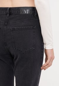 Black denim jeans with a fitted shape, featuring a VMD leather label on the waistband and two back pockets with stitched borders.