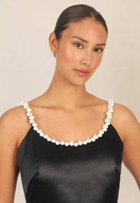 Schwarzes Satinkleid mit rundem Halsausschnitt, verziert mit weißen Perlen, das eine glatte Textur und ein elegantes Design zeigt.