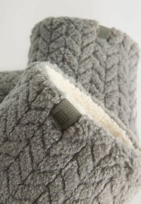 Grå fleece-hjemmesko med en tekstureret overflade, cremefarvet indvendig foring og en lille grå labeldetalje på siden.