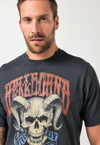Camiseta gráfica negra con un skull y cuernos de carnero. El diseño tiene acentos en naranja y azul con el texto "HELLBOUND" en una fuente bold.