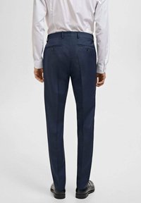 Navy trousers with a slim fit, featuring two back pockets, a smooth texture, and subtle crease lines along the legs, paired with black shoes.