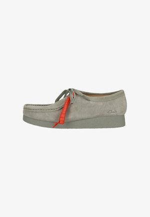 Grijze suede schoen met een ronde neus, voorzien van een contrasterend rood veter en een gestructureerde zool. Merken zijn in de zijkant geperst.