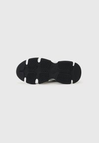 Black athletic shoe sole with textured rubber for grip, featuring a wavy pattern and a rounded toe design. Two white accents near the heel.