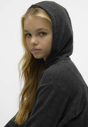 Mörkgrå huvtröja med mjuk textur. Huvan är något neddragen, vilket avslöjar långt, rakt hår. Enkel design utan synliga logotyper.