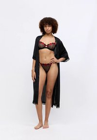 Svart blonder-kimono over gjennomsiktig svart BH og matchende truse med røde blomsterdetaljer, som fremhever delikat stoff og intrikate designdetaljer.