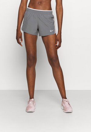 Sportler trägt graue Nike-Laufshorts und pinke Laufschuhe und steht vor einem schlichten, hellen Hintergrund.
