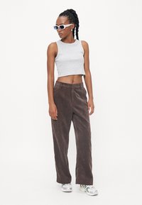 Grijze cropped tanktop gecombineerd met bruine corduroy wijde broek. Model draagt witte zonnebril en zilveren sneakers. Minimalistisch ontwerp en texturen.