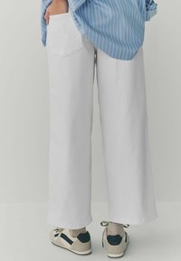 Witte katoenen broek met brede pijpen en een achterzak. Gecombineerd met een blauw gestreept shirt en casual sneakers, met neutrale sokken.