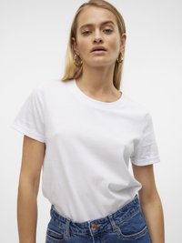 Hvit bomulls t-skjorte med rund hals og korte ermer, kombinert med høy midje blå jeans, med knappelukking og denim tekstur.