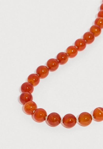 Mărgele late, rotunde și lucioase, de culoare chihlimbar, șiruite într-un colier curbat pe un fundal alb simplu.